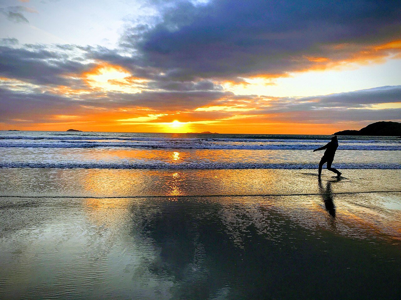 Person skimming stones at a beach during sunset