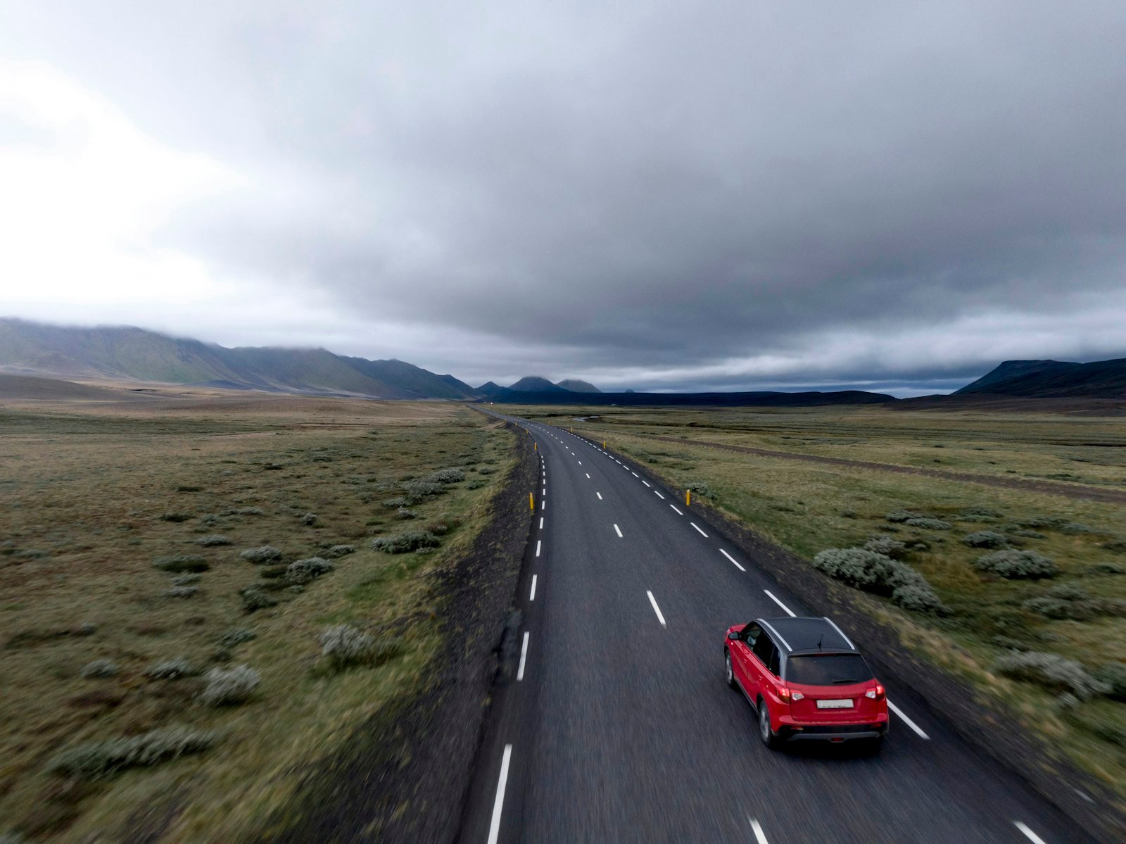 Red hatchback car parked on an asphalt road in Iceland
