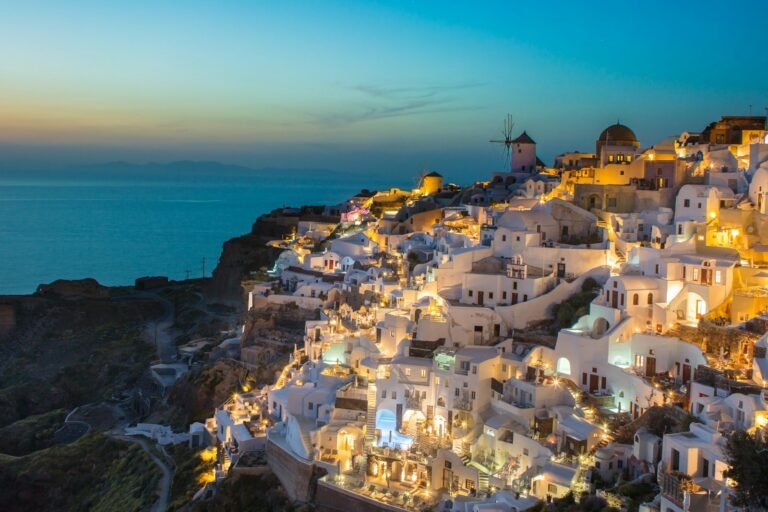 White buildings on a cliffside in Oia, Greece, illuminated by warm evening light
