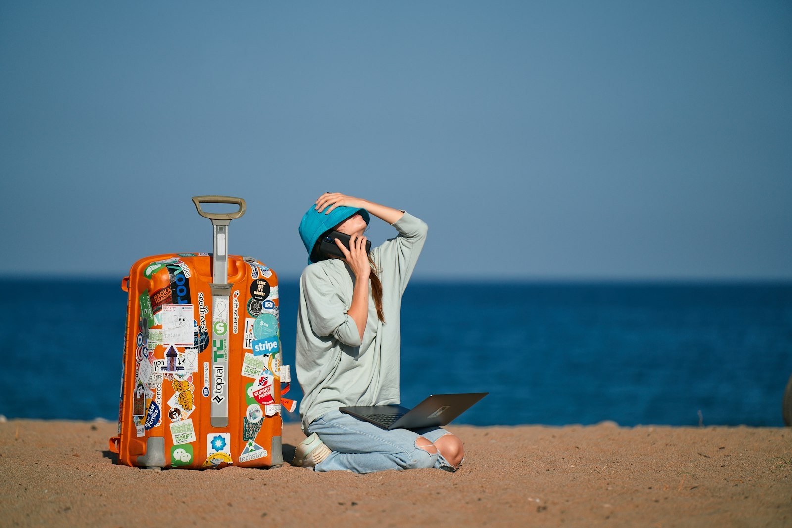 A person sitting on a beach with a suitcase and a laptop