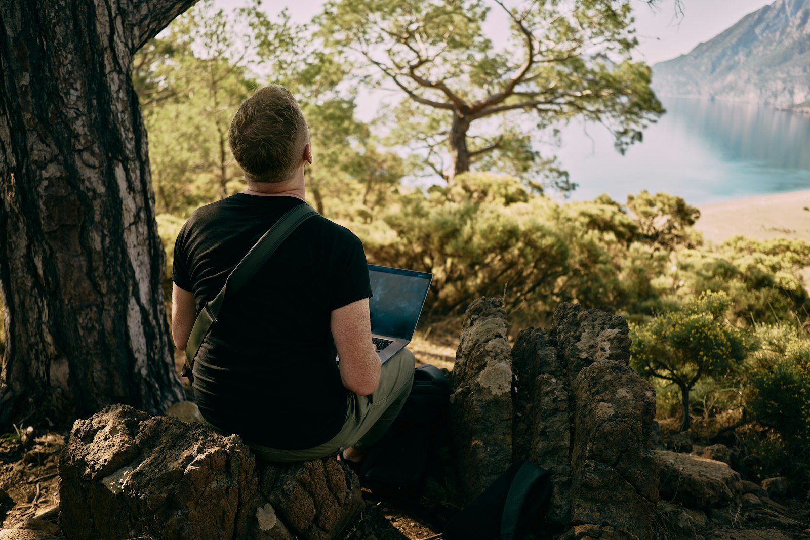 A man sitting on a rock with a laptop in his lap