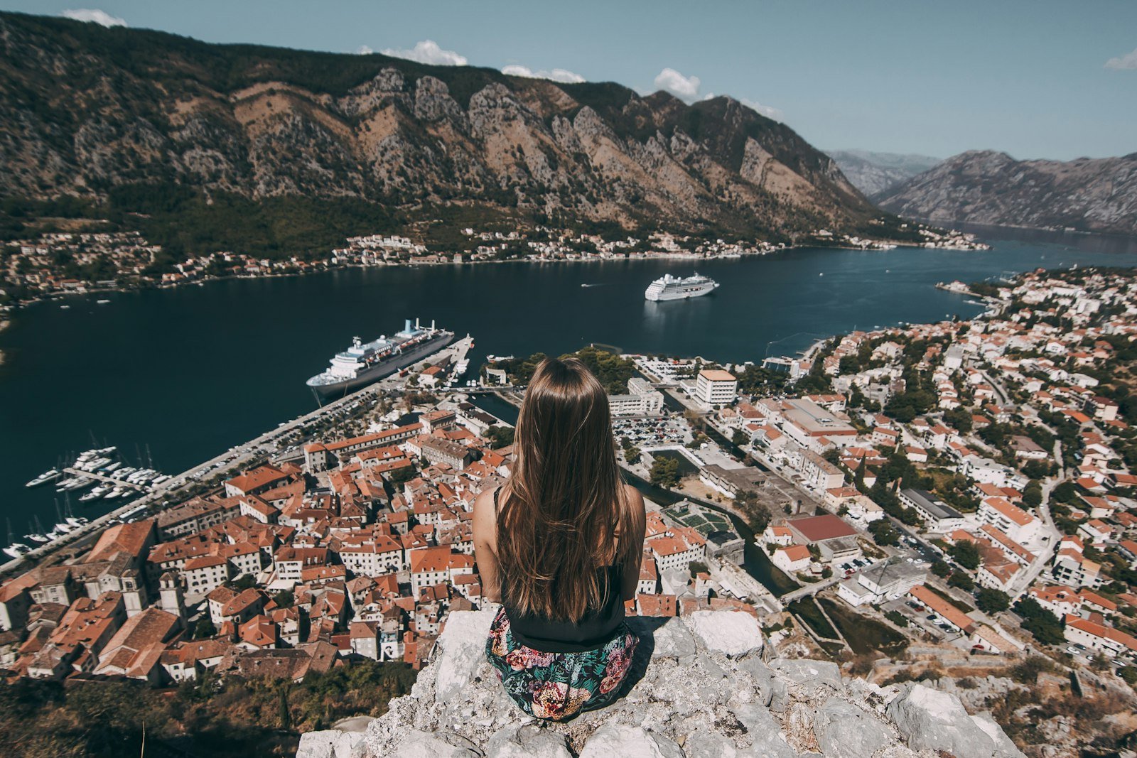 Woman sitting on top of cliff facing buildings in Kotor, Montenegro